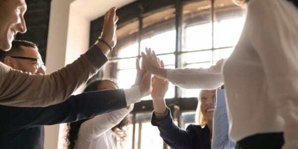 Overjoyed older and younger teammates joining hands in air, giving high five, celebrating shared company success in business meeting. Happy diverse colleagues coming to common decision, showing unity.